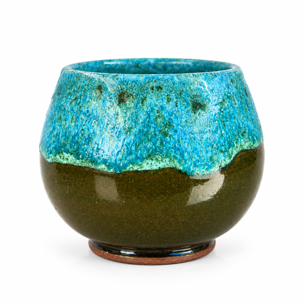 Tasse arrondie en céramique émaillée turquoise et marron, avec une anse ronde, posée sur une table en bois.