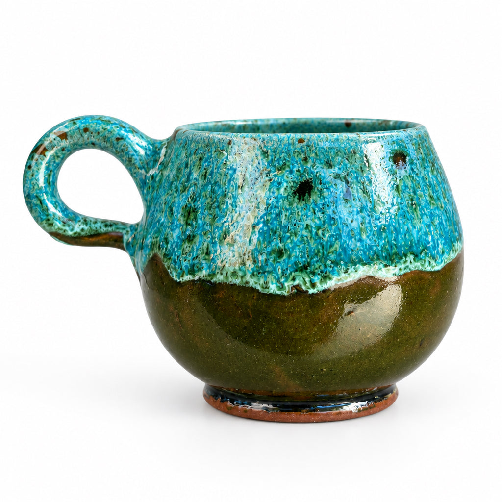Tasse arrondie en céramique émaillée turquoise et marron, avec une anse ronde, posée sur une table en bois.