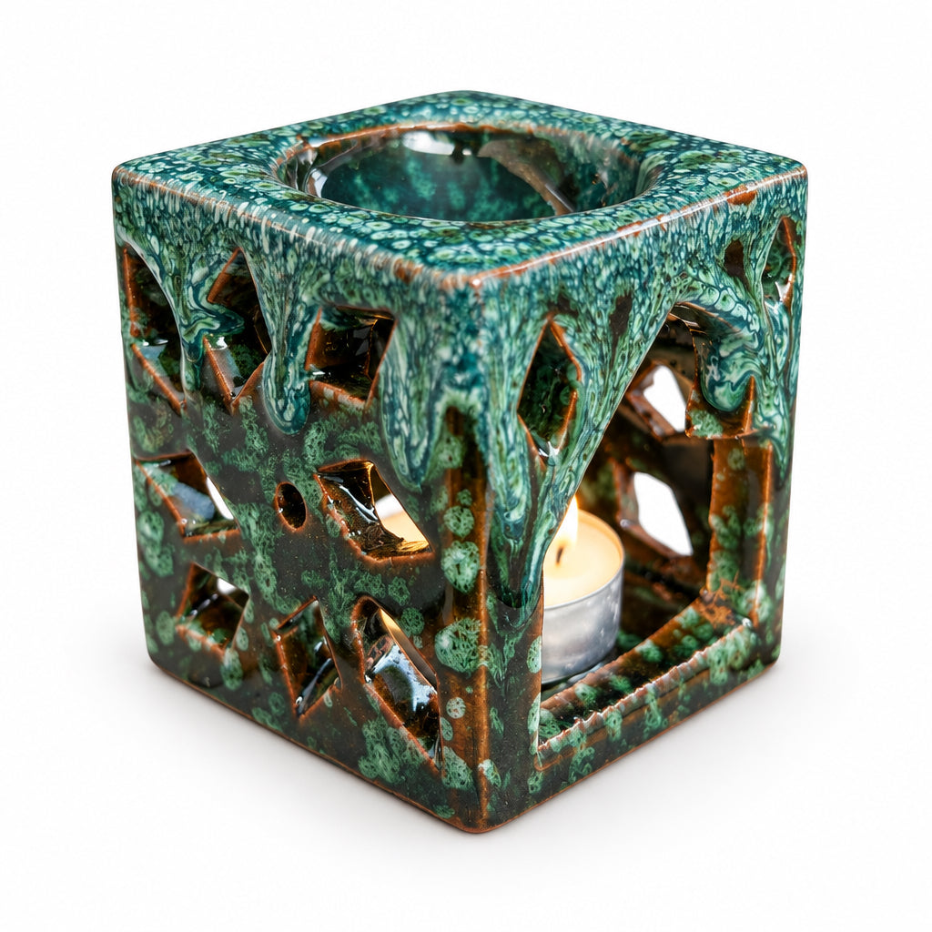 Brûle-parfum carré en céramique vert émeraude et marron, avec finition mouchetée, motifs ajourés en losanges et bougie chauffe-plat allumée à l’intérieur.