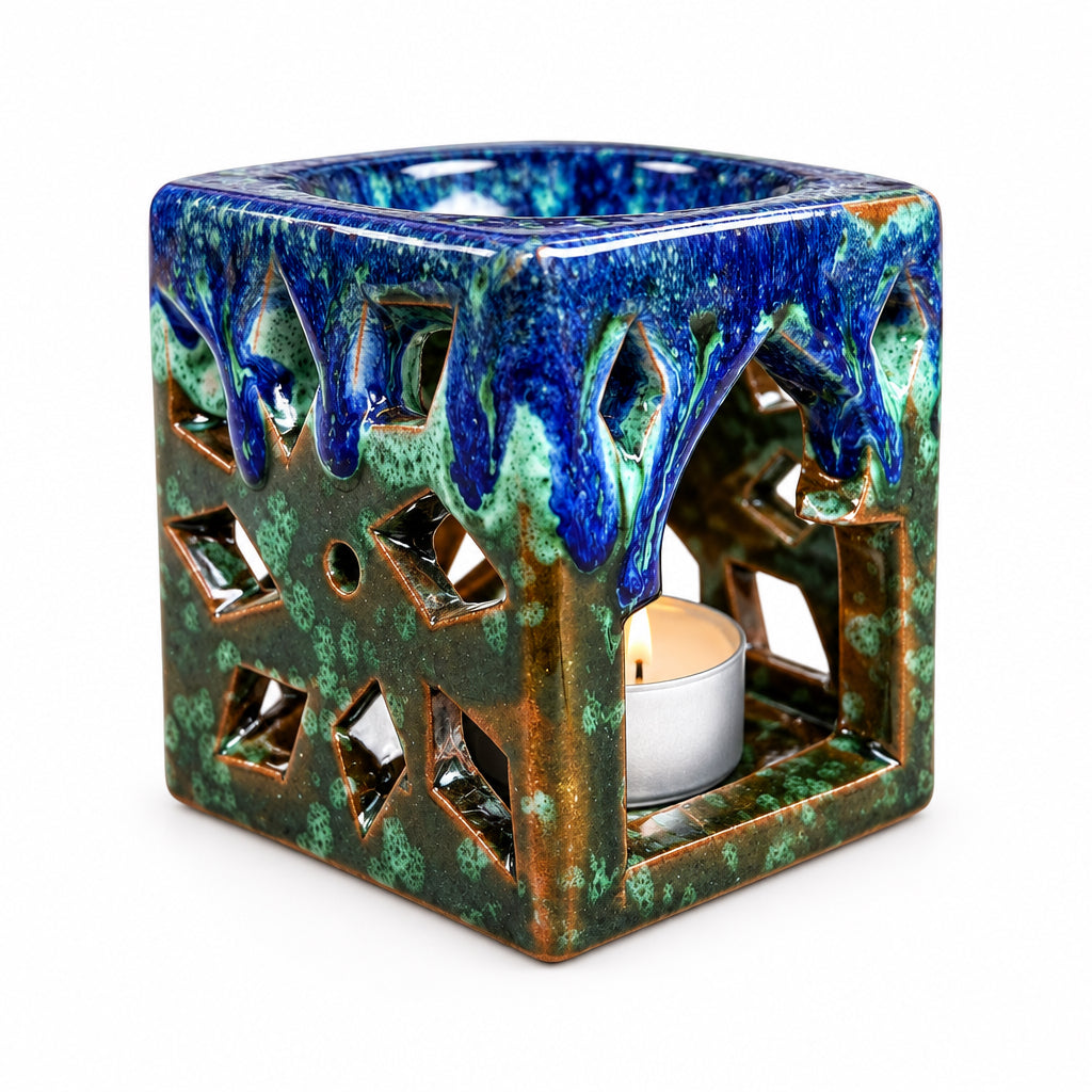 Brûle-parfum carré en céramique bleu marine, marron et vert, avec finition mouchetée, motifs ajourés et bougie chauffe-plat à l’intérieur.