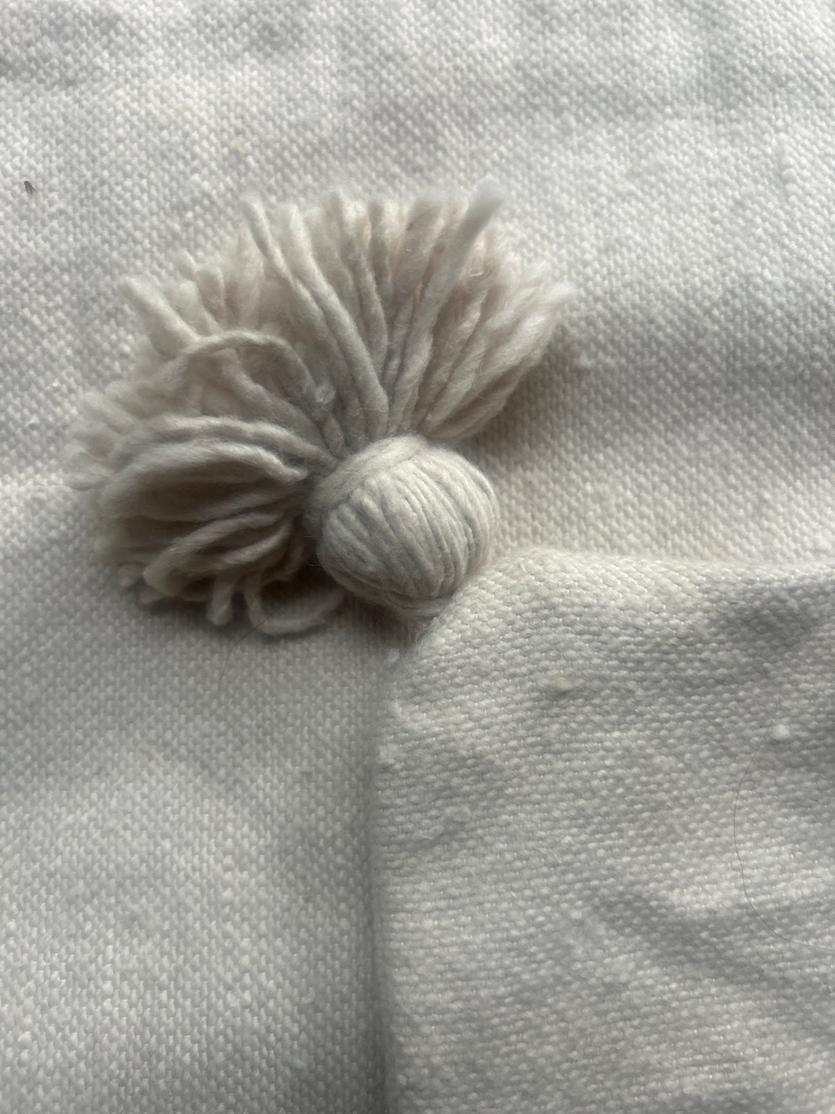 Détail pompon en coton naturel écru d'un coussin artisanal marocain – finition fait main de qualité
