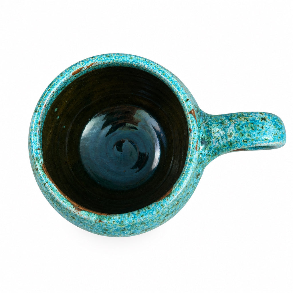 Tasse arrondie en céramique émaillée turquoise et marron, avec une anse ronde, posée sur une table en bois.