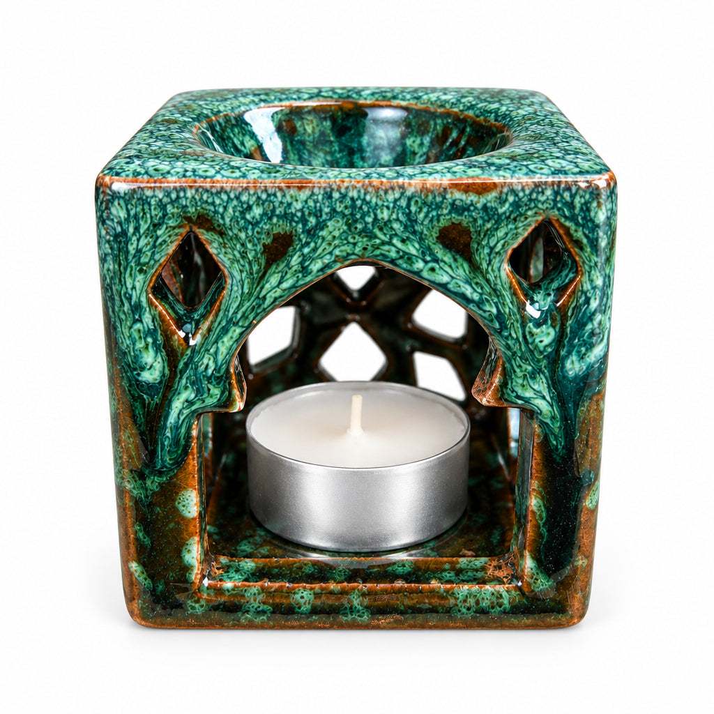 Brûle-parfum carré en céramique vert émeraude et marron, avec finition mouchetée, motifs ajourés en losanges et bougie chauffe-plat allumée à l’intérieur.
