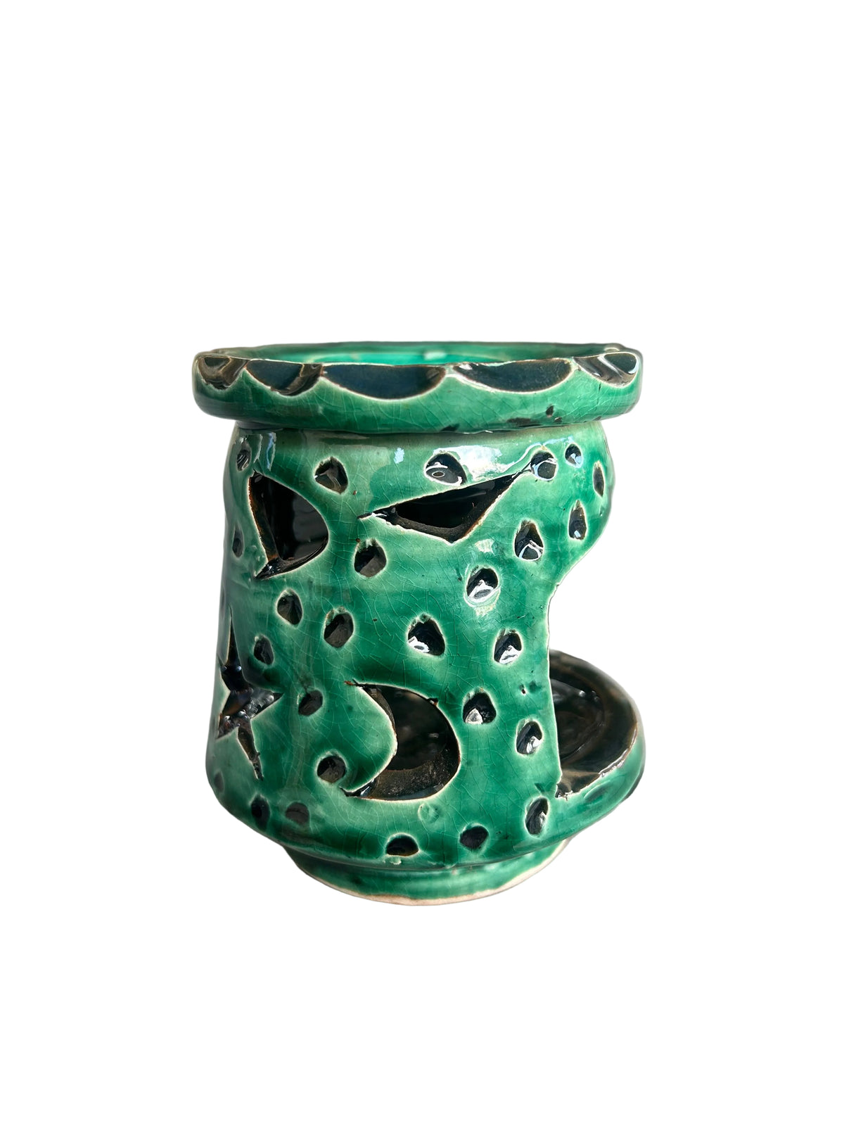 Brûle-parfum en céramique vert foncé brillant, avec lunes et étoiles ajourées, coupelle à bord ondulé et bougie chauffe-plat allumée.