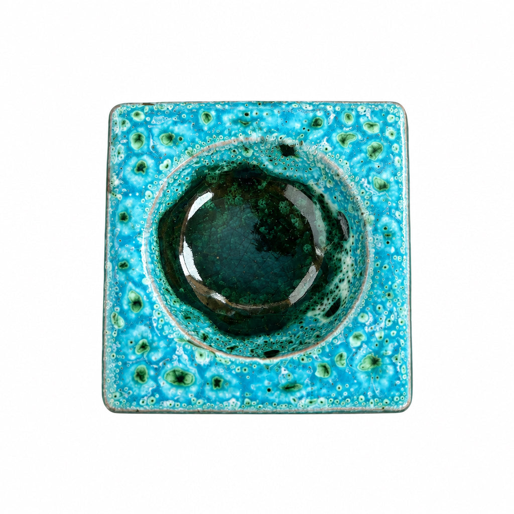 Brûle-parfum carré en céramique bleu turquoise, vert et marron, avec finition mouchetée, motifs ajourés et bougie chauffe-plat à l’intérieur.