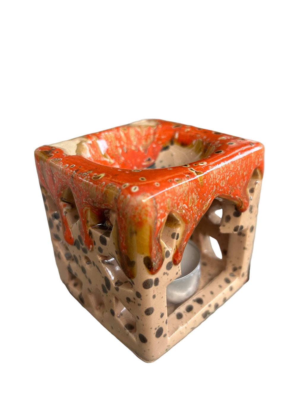 Brûle-parfum carré en céramique crème mouchetée et orange, avec motifs ajourés et bougie chauffe-plat à l’intérieur. 