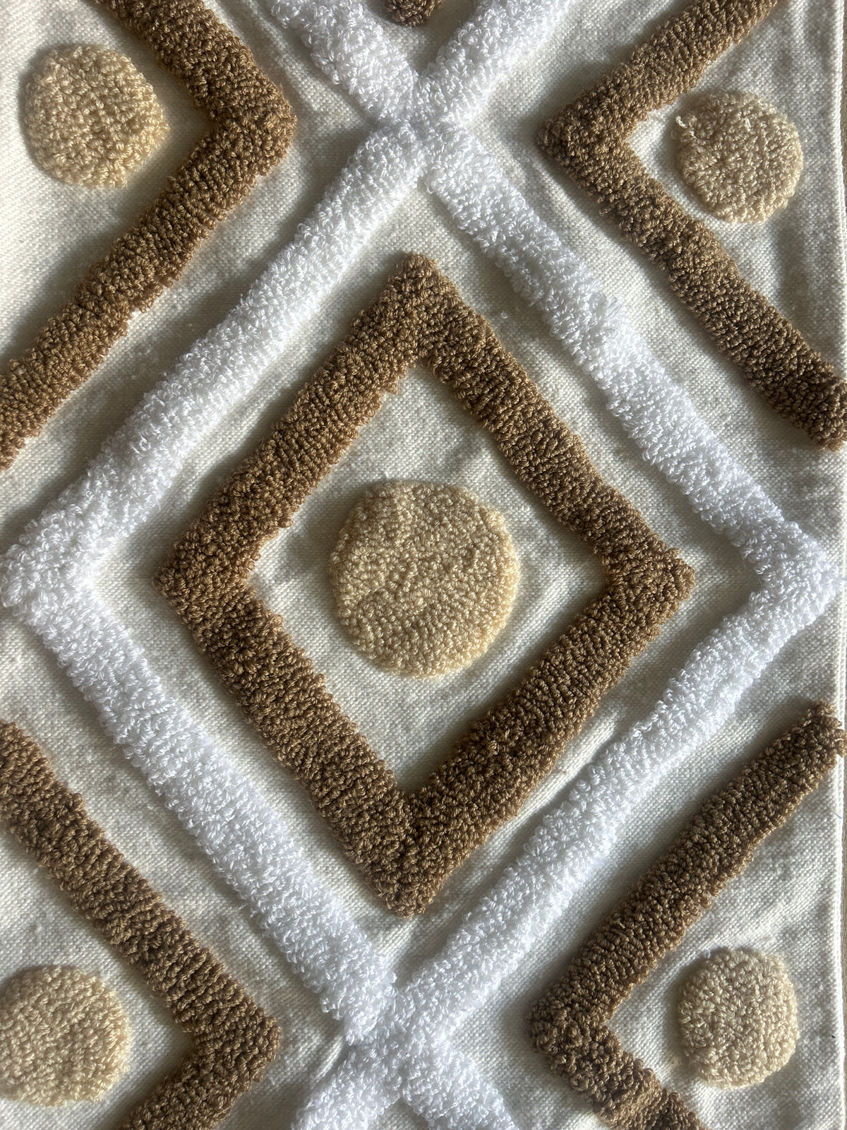  Gros plan sur le tissu : motifs géométriques berbères en relief très nets — losanges imbriqués, médaillons ronds, lignes croisées en coton touffeté camel et blanc écru. Idéal pour montrer la texture et la qualité artisanale.