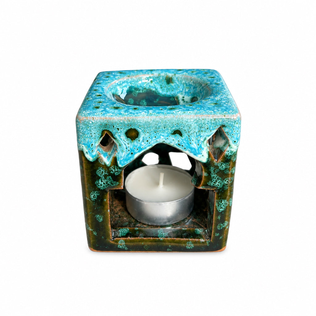 Brûle-parfum carré en céramique bleu turquoise, vert et marron, avec finition mouchetée, motifs ajourés et bougie chauffe-plat à l’intérieur.
