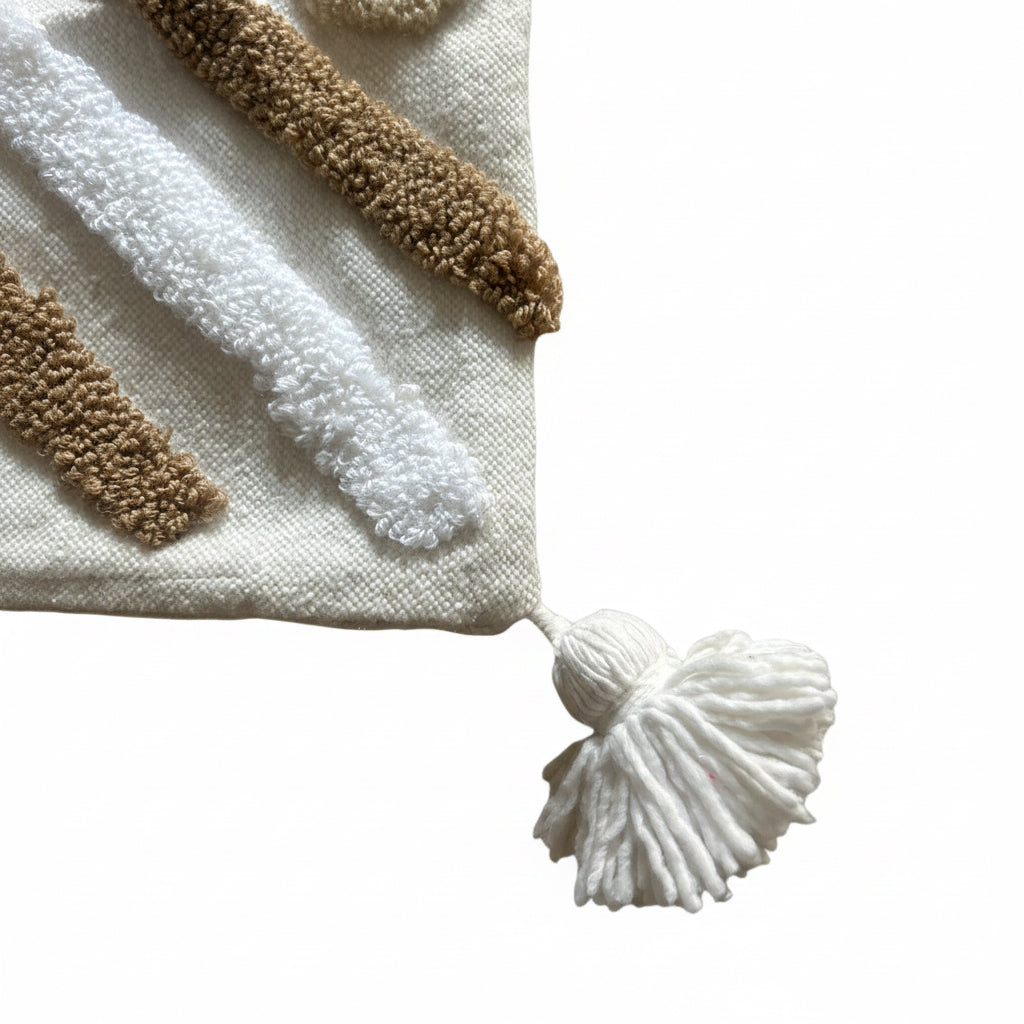 "Gros plan sur le coin de la housse de coussin XL berbère — pompon en coton blanc et motifs touffetés bicolores blanc et camel, finition artisanale marocaine fait main"