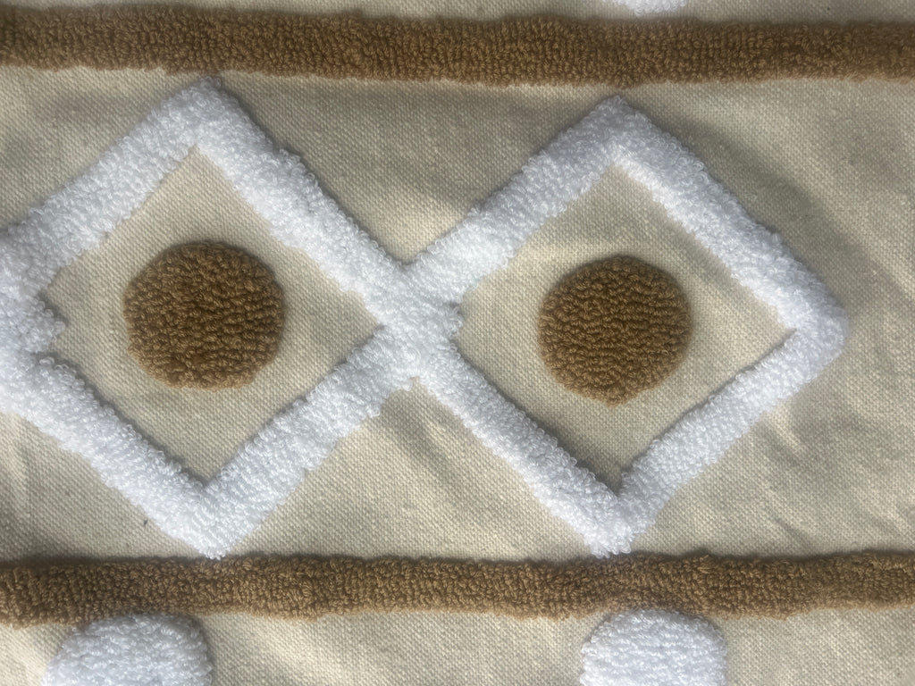 Zoom sur broderie tufté artisanale : losanges blancs et médaillons caramel sur fond écru – détail coussin marocain fait main