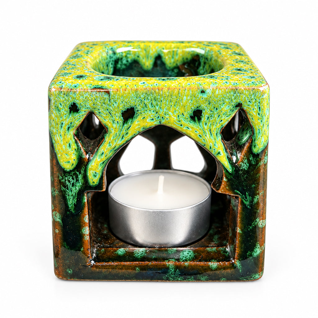 Brûle-parfum carré en céramique verte et marron, avec finition mouchetée, motifs ajourés et bougie chauffe-plat allumée.