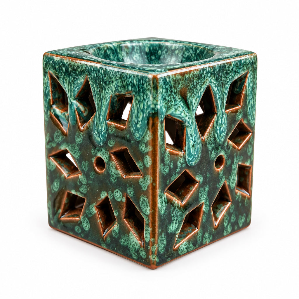 Brûle-parfum carré en céramique vert émeraude et marron, avec finition mouchetée, motifs ajourés en losanges et bougie chauffe-plat allumée à l’intérieur.