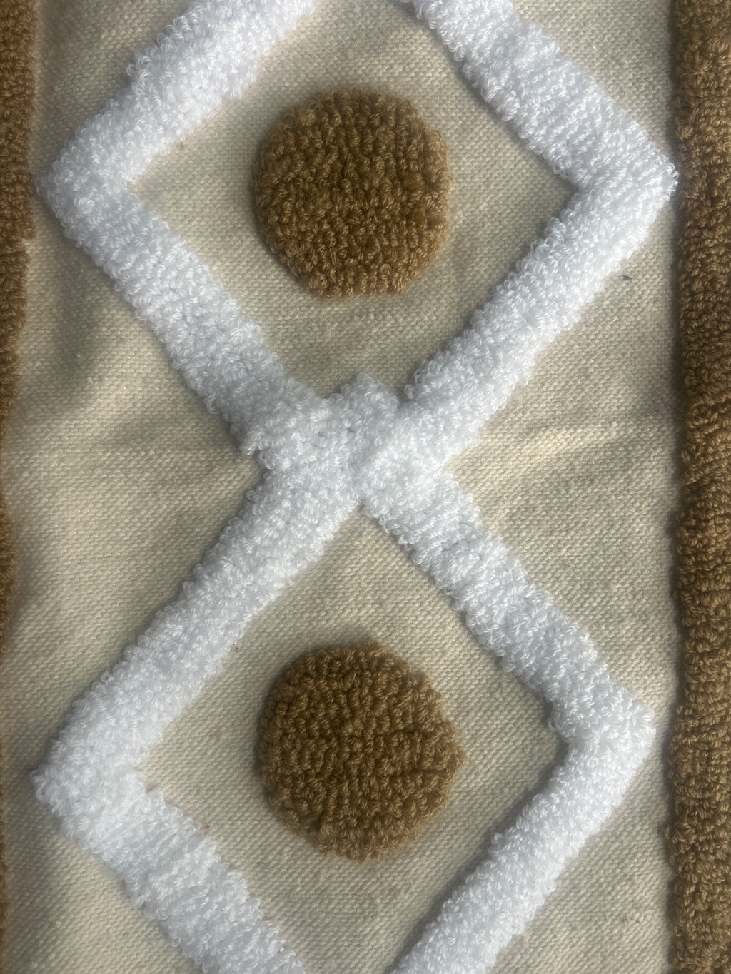 Gros plan sur la texture tufté d'un coussin marocain : motifs losanges blancs et ronds caramel sur fond naturel 