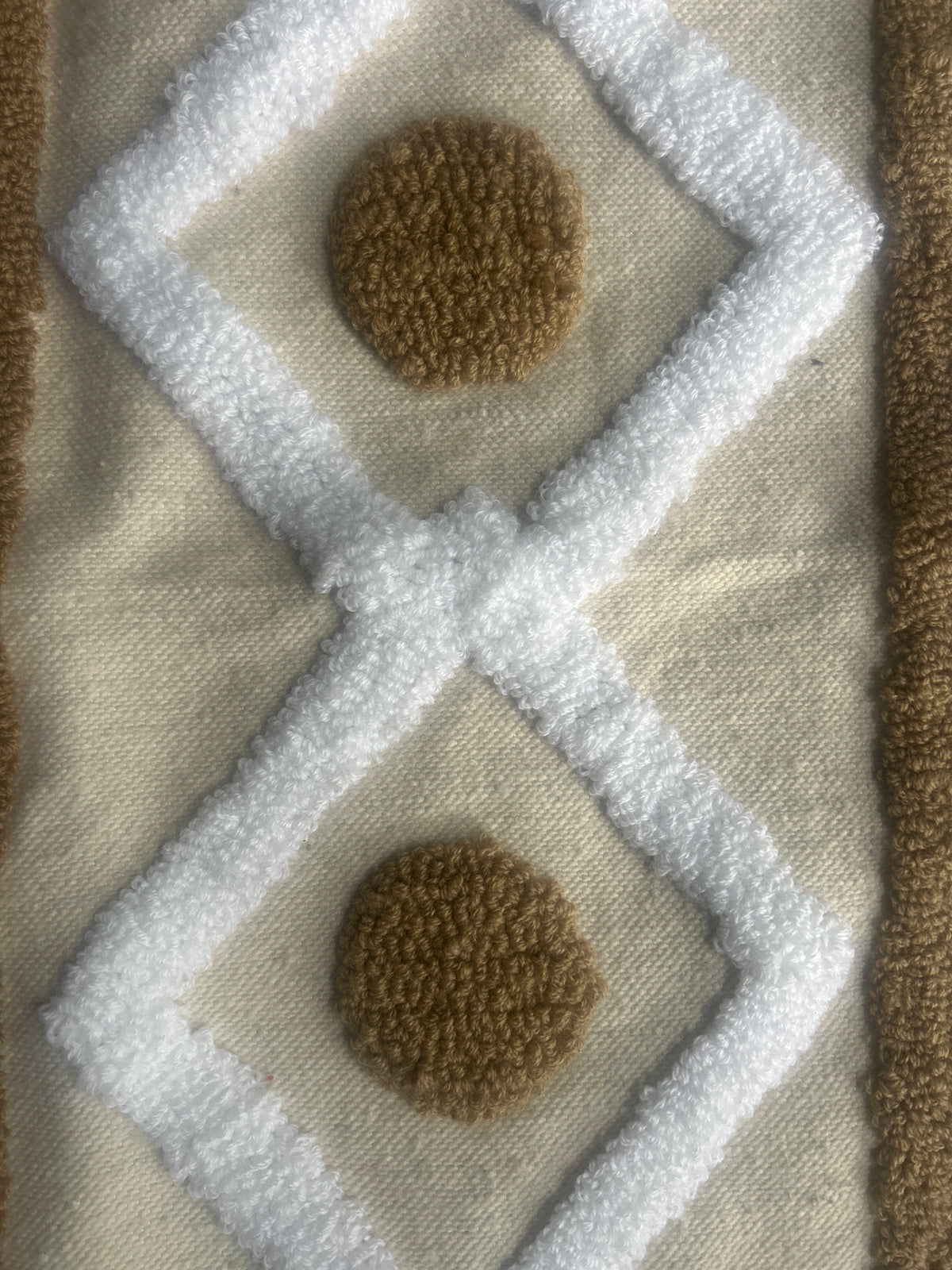 Gros plan sur la texture tufté d'un coussin marocain : motifs losanges blancs et ronds caramel sur fond naturel 