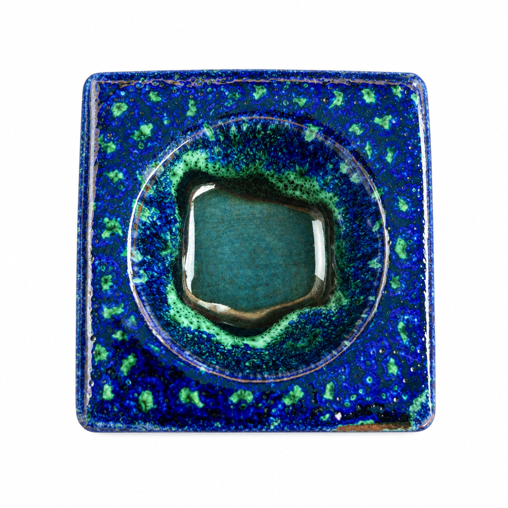 Brûle-parfum carré en céramique bleu marine, marron et vert, avec finition mouchetée, motifs ajourés et bougie chauffe-plat à l’intérieur.