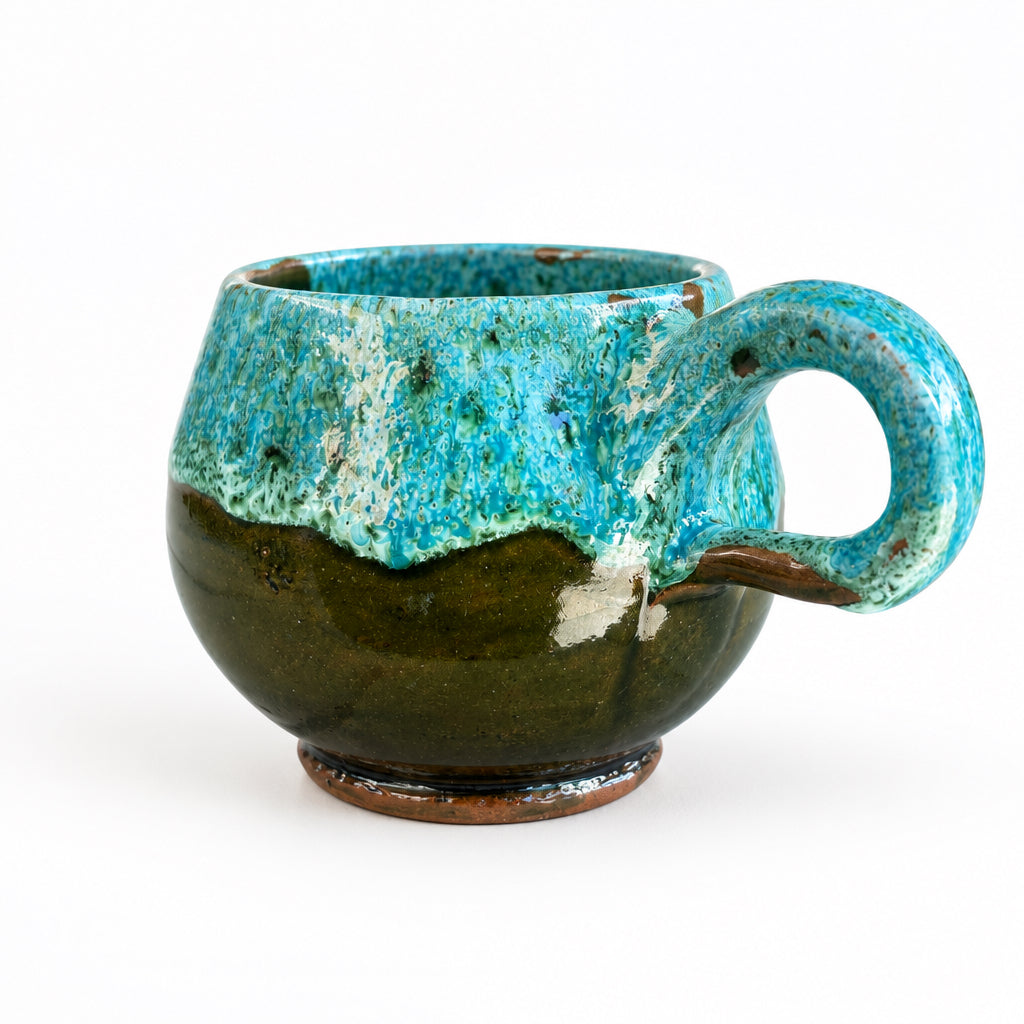 Tasse arrondie en céramique émaillée turquoise et marron, avec une anse ronde, posée sur une table en bois.