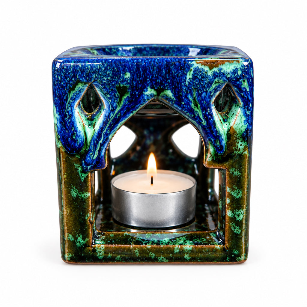 Brûle-parfum carré en céramique bleu marine, marron et vert, avec finition mouchetée, motifs ajourés et bougie chauffe-plat à l’intérieur.