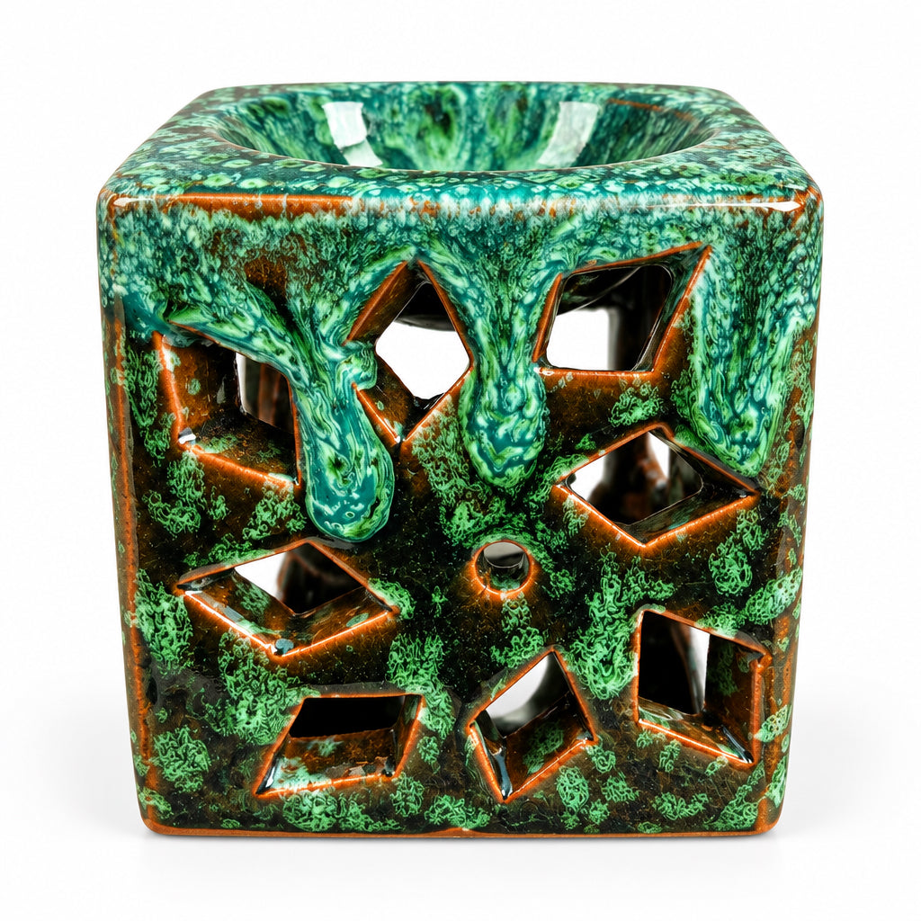Brûle-parfum carré en céramique vert émeraude et marron, avec finition mouchetée, motifs ajourés en losanges et bougie chauffe-plat allumée à l’intérieur.