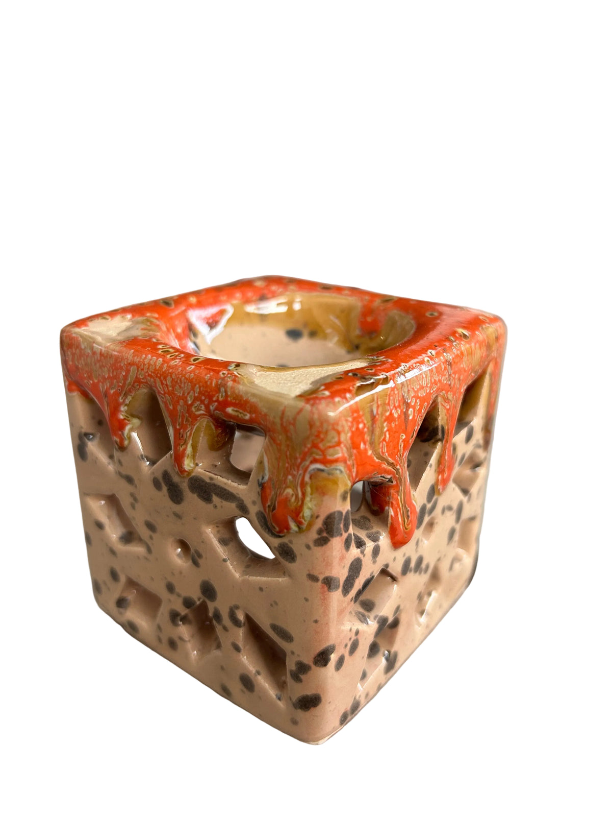 Brûle-parfum carré en céramique crème mouchetée et orange, avec motifs ajourés et bougie chauffe-plat à l’intérieur. 
