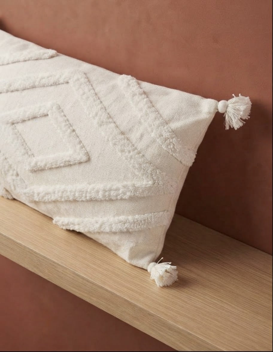 Gros plan housse de coussin XXL blanc naturel – tissage berbère relief fait main avec pompons – posée sur étagère bois fond terracotta