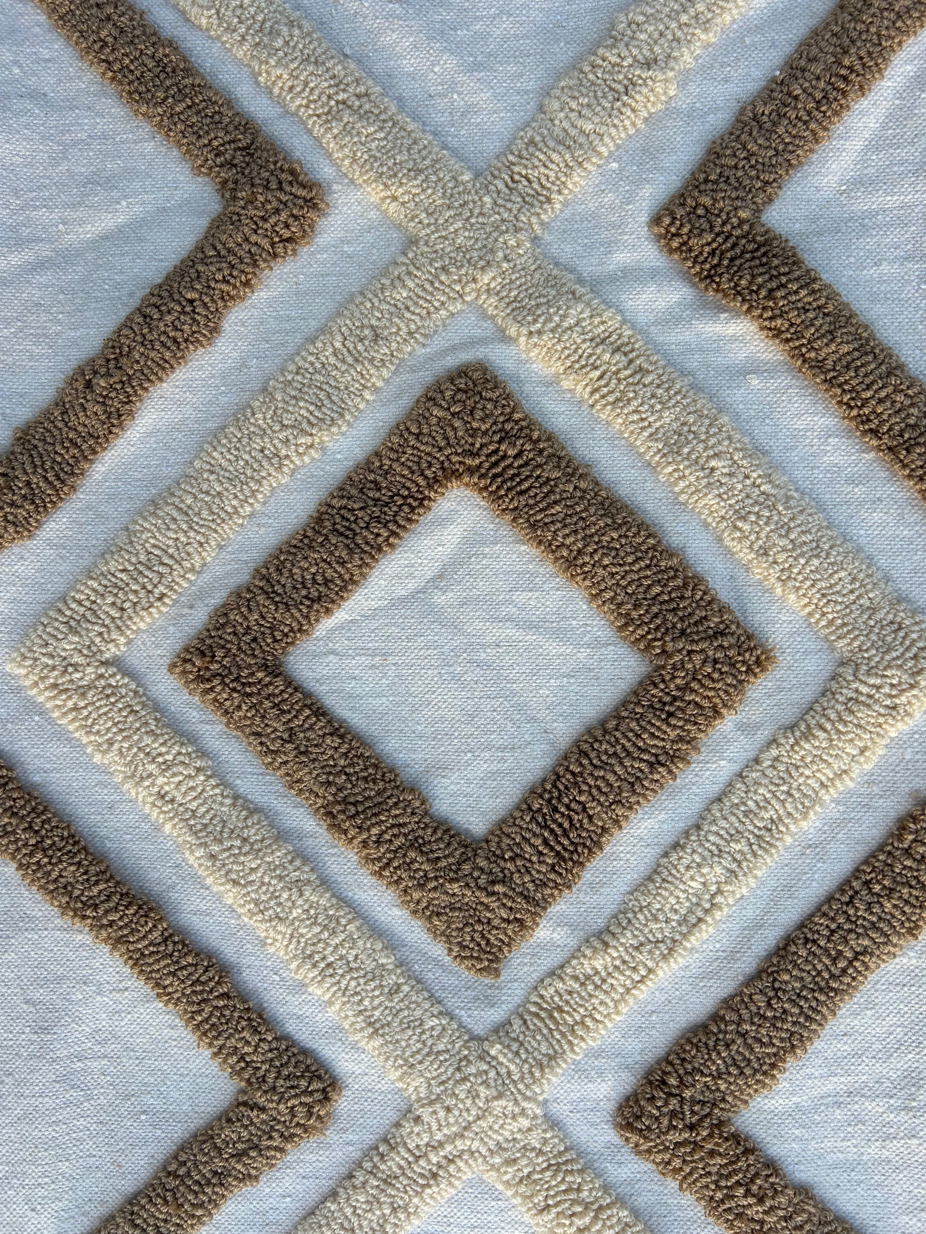 "Gros plan sur le motif touffeté berbère de la housse de coussin XL — losanges imbriqués en relief bicolore camel et blanc, coton tissé main au Maroc"