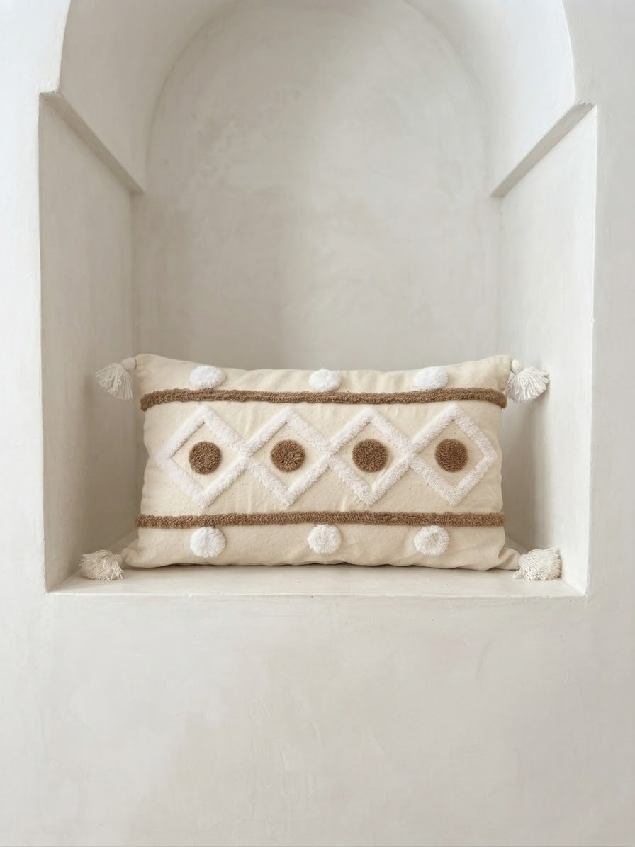 Coussin rectangulaire artisanal écru à broderies géométriques et franges, style marocain minimaliste, posé dans une niche en stuc blanc