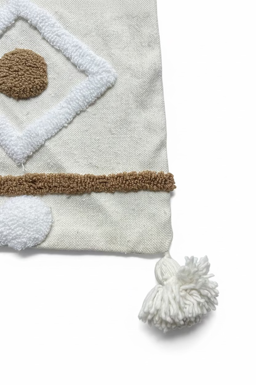 Détail coin housse de coussin berbère XL, pompon en coton ivoire et bande camel bouclée en lisière, fait main au Maroc