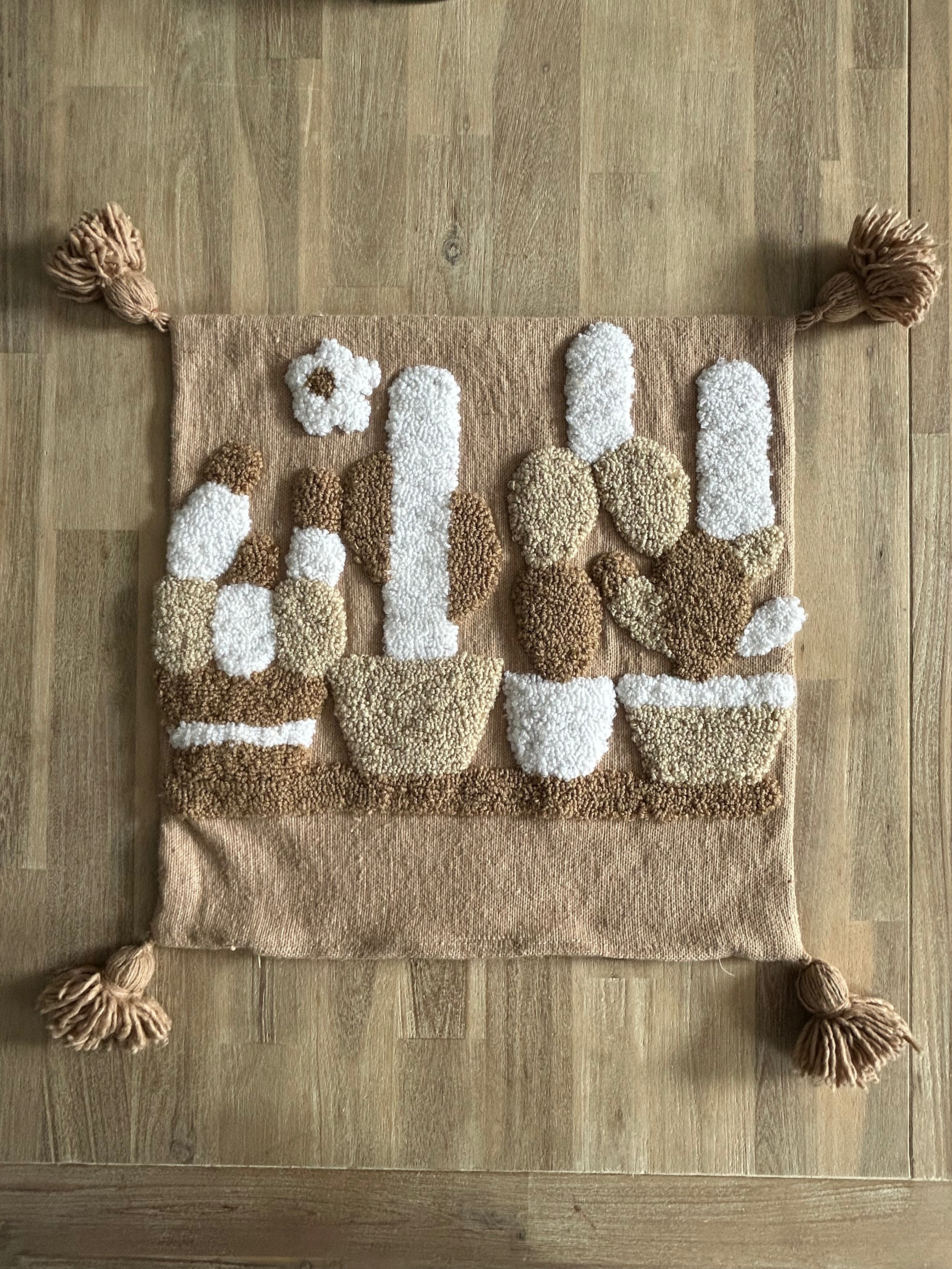  Housse de coussin berbère punch needle abstraite 48x48 cm, tons sable et ivoire, pompons camel, posée sur table en bois dans un riad marocain
