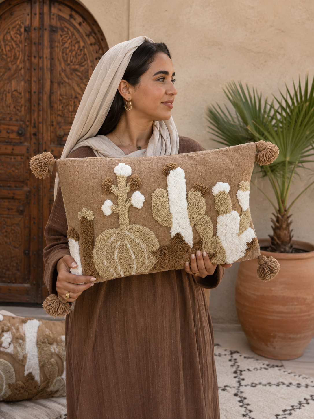  Femme en tenue traditionnelle marocaine tenant une housse de coussin punch needle cactus berbère 62x40 cm avec pompons
