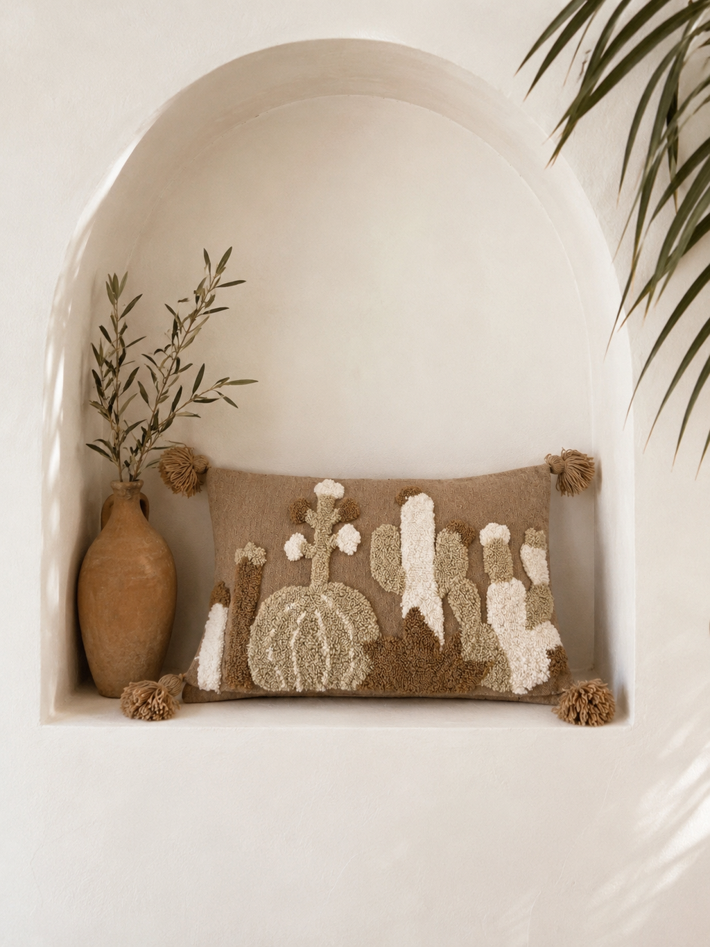  Housse de coussin artisanale punch needle motif cactus du désert, présentée dans une niche murale blanche style architecture marocaine
