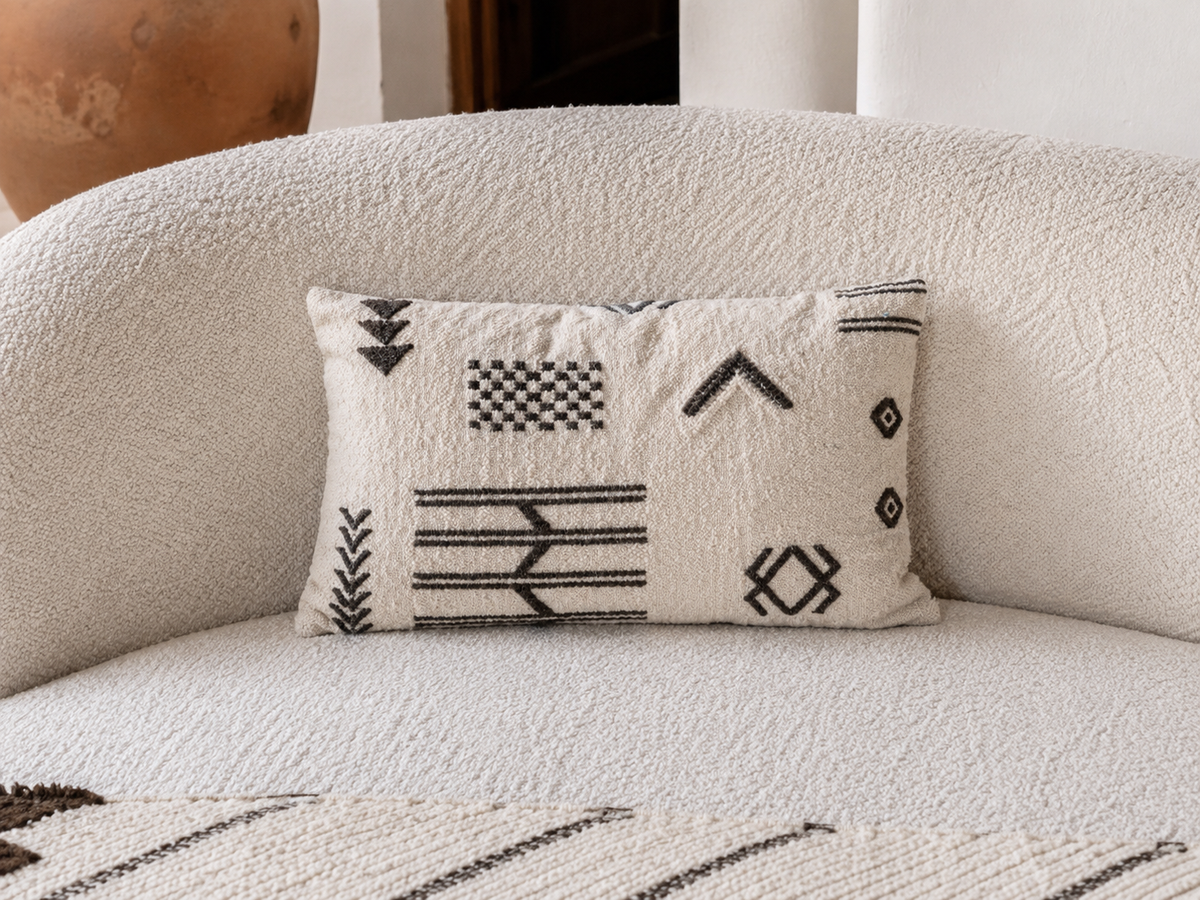 Coussin berbère ivoire et noir sur canapé boucle blanc – motifs graphiques flèches et losanges marocains