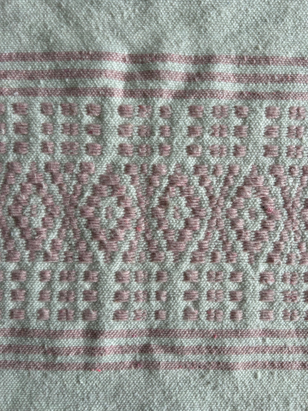 Gros plan broderie berbère marocaine – motifs floraux rose poudré tissés à la main