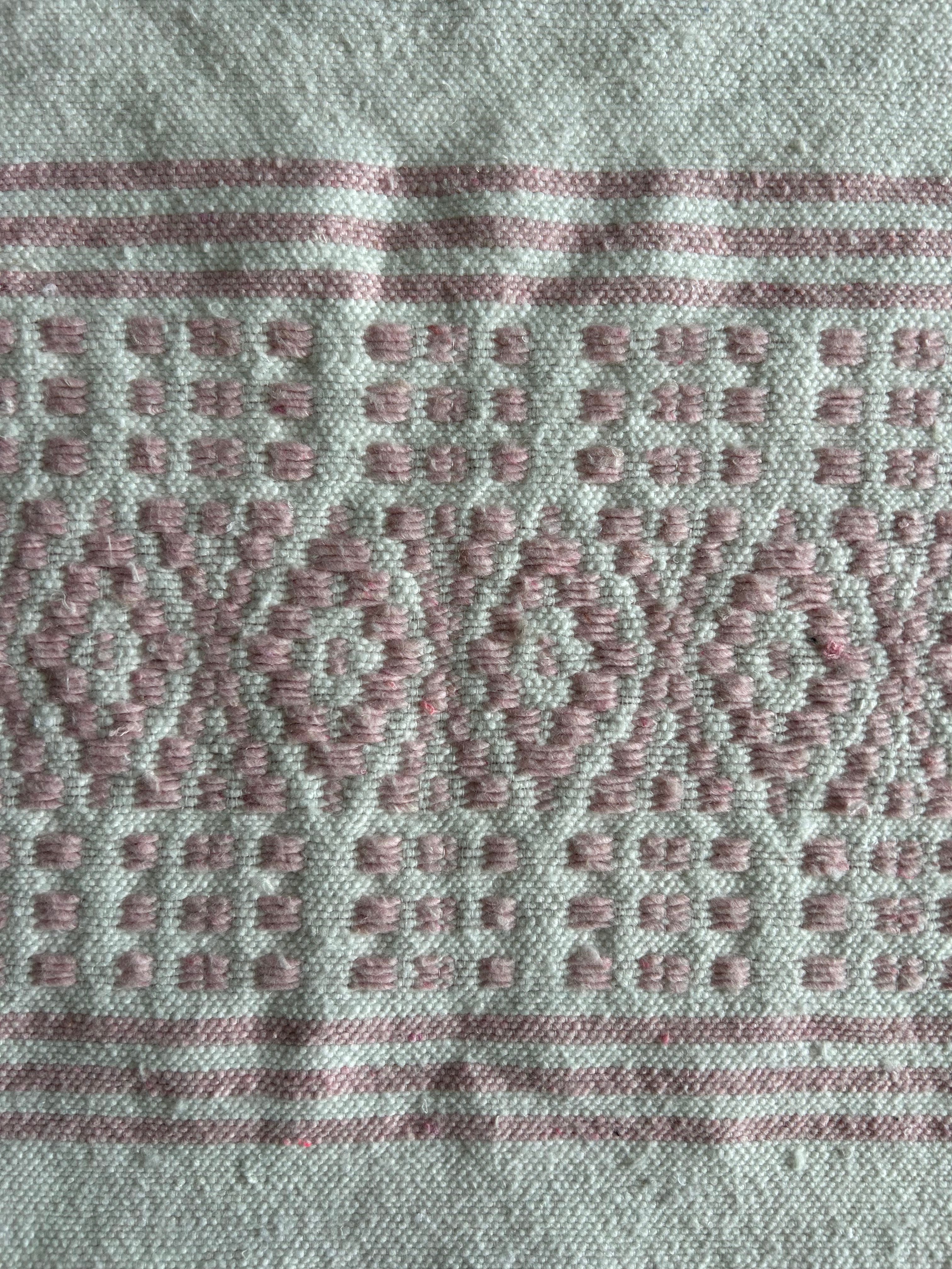 Gros plan broderie berbère marocaine – motifs floraux rose poudré tissés à la main