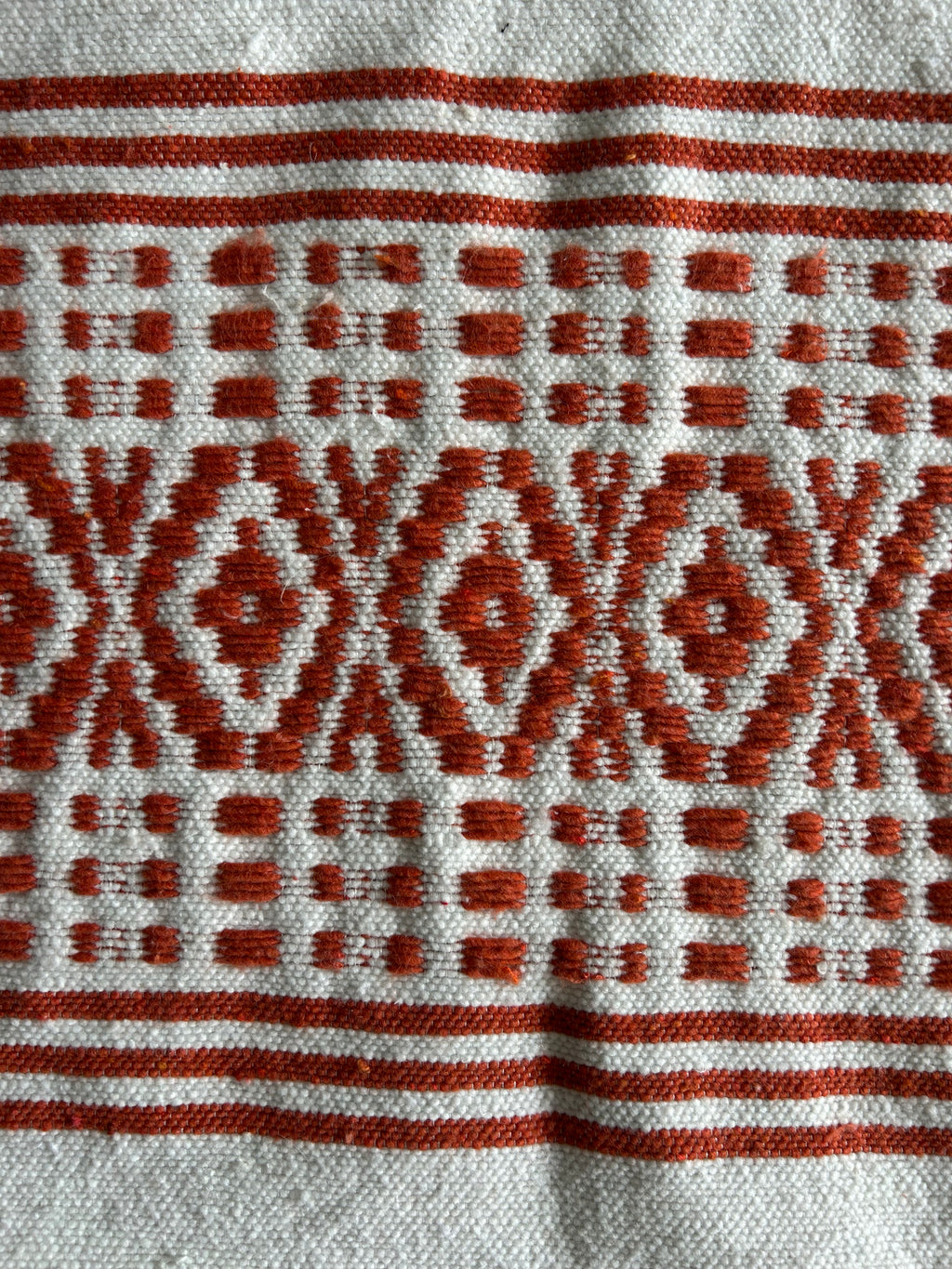 Gros plan tissage berbère marocain – motifs géométriques terracotta et ivoire faits main