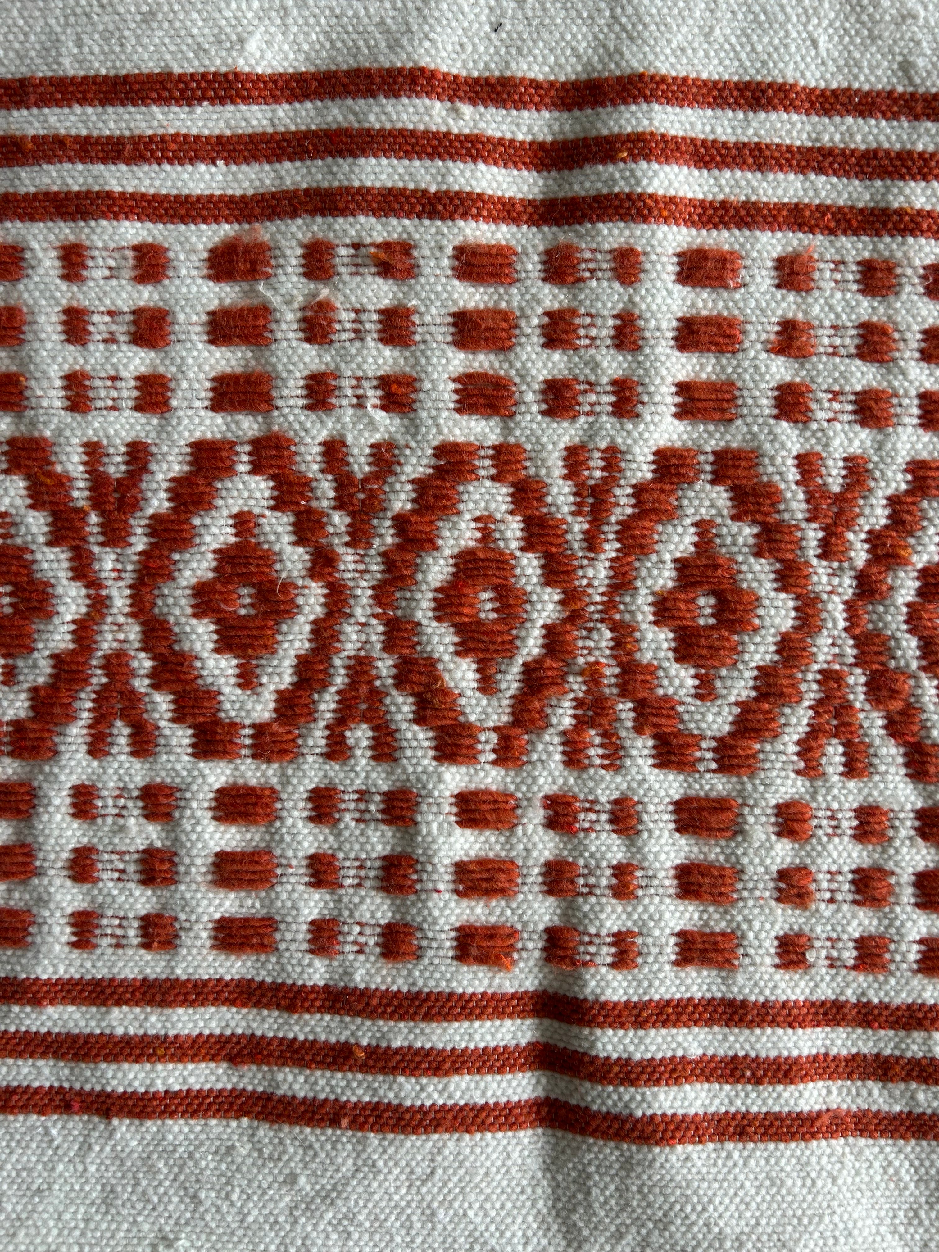 Gros plan tissage berbère marocain – motifs géométriques terracotta et ivoire faits main