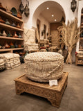 Pouf berbère en laine pure tissée main, posé sur un présentoir en bois sculpté dans une boutique artisanale marocaine