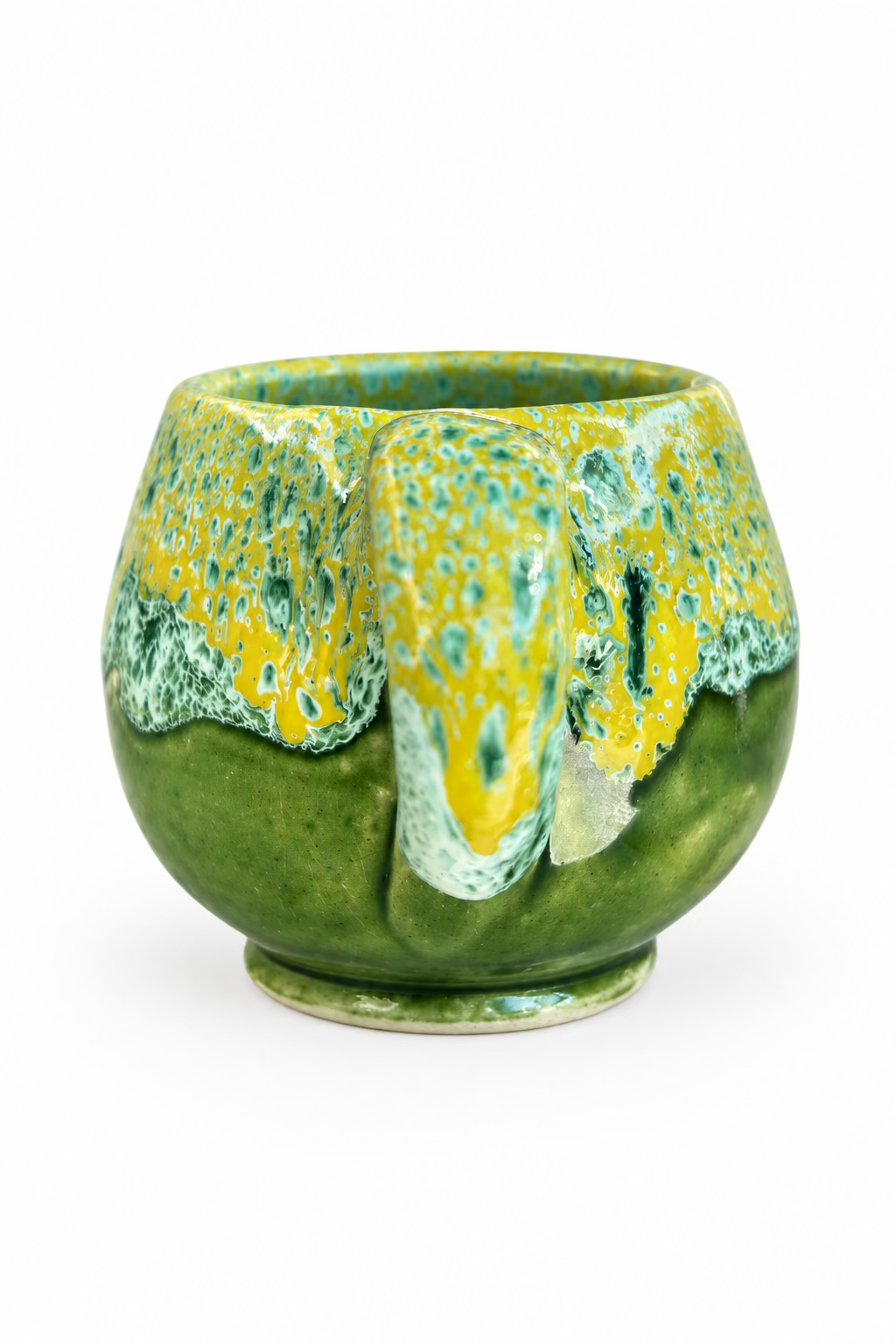 Tasse arrondie en céramique verte et jaune, avec anse incurvée, finition brillante et effets mouchetés turquoise sur la partie supérieure.